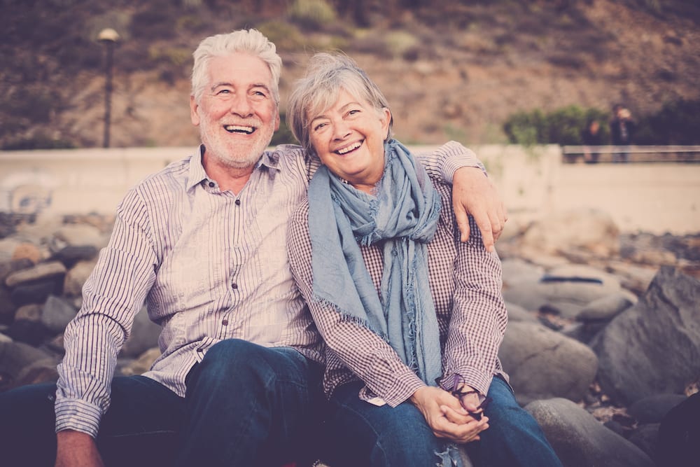 Happy elderly couple sitting on a beach smiling